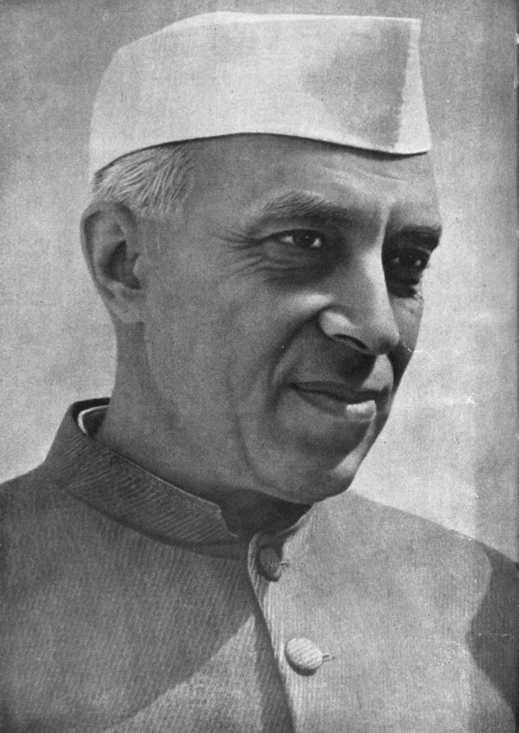 Jawaharlal Nehru in a white cap and buttoned jacket, smiling to one side